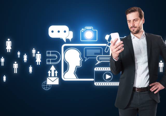 Hombre de negocios usando un smartphone frente a una composición de iconos digitales que representan comunicación, marketing y redes sociales, en un entorno tecnológico de tonos azules