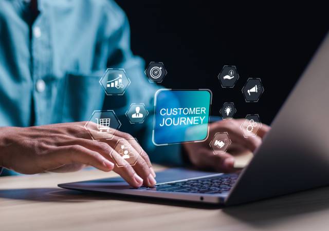 Persona usando una computadora portátil con una gráfica digital que muestra el texto «CUSTOMER JOURNEY» e íconos de marketing